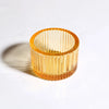 A clear amber glass votive holder with vertical fluting, used as a tealight candle holder.