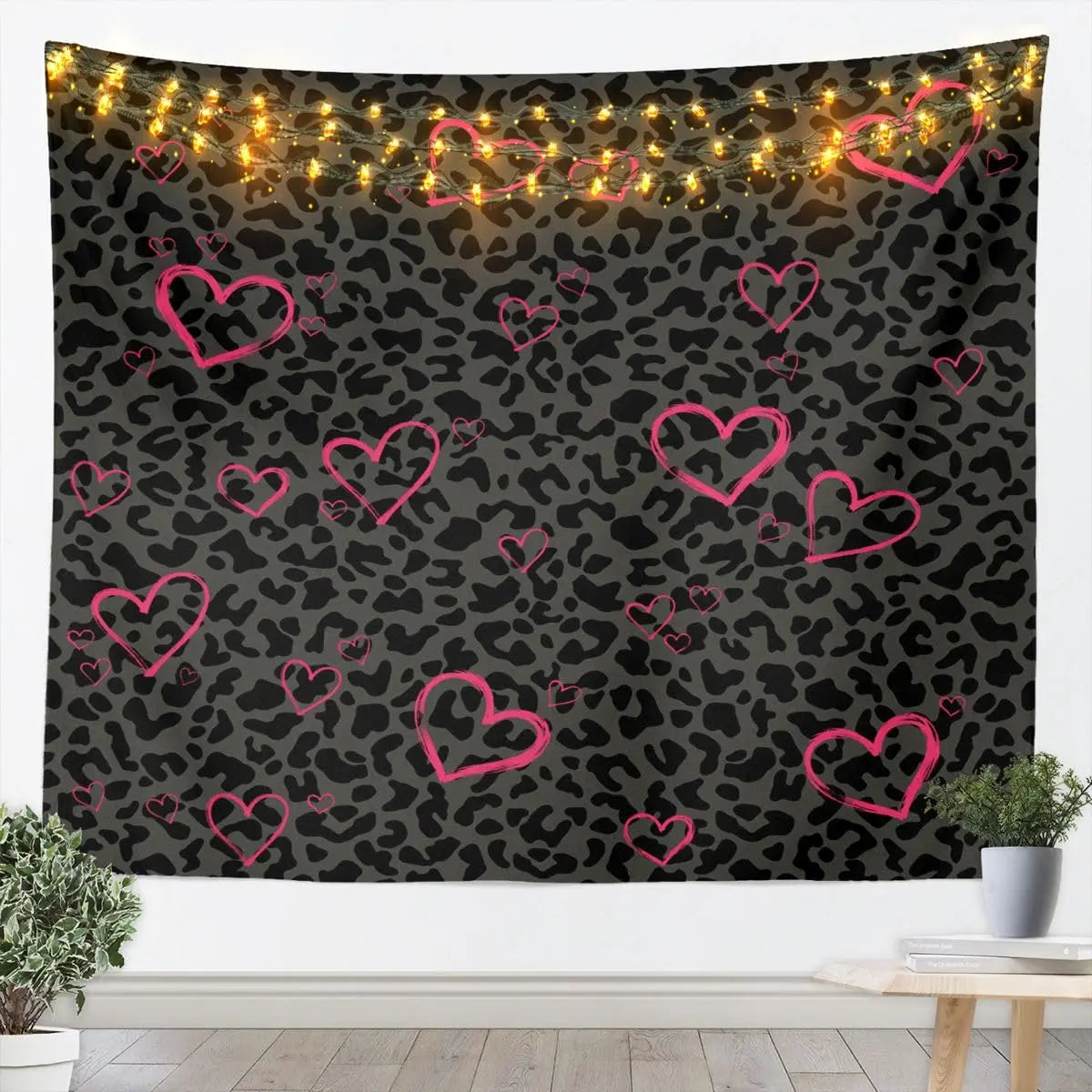 A dark tapestry wall hanging featuring a leopard print pattern with warm string lights outlining pink hearts.