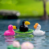 Trois petites sculptures animales en résine d'oiseaux roses, noirs et blancs flottant sur l'eau.