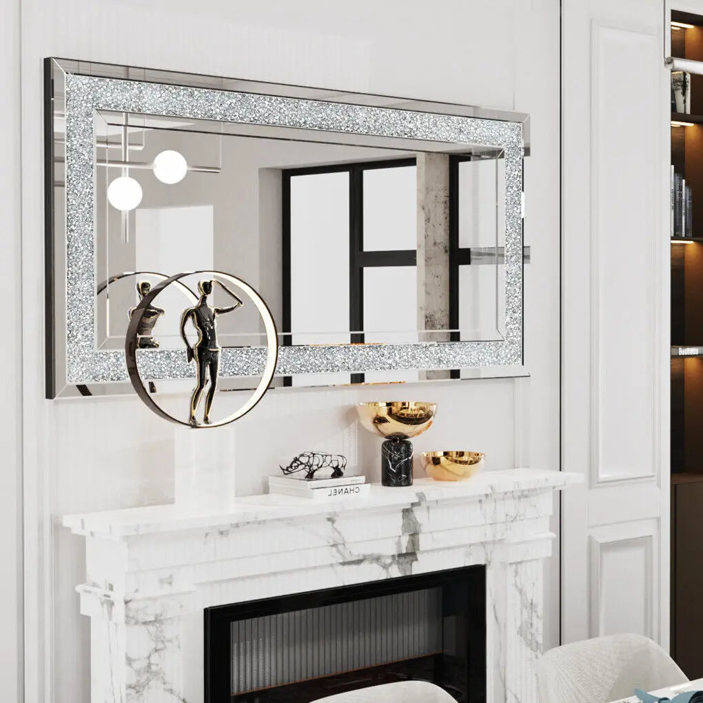A silver crystal rhinestone wall mirror with a sparkling frame displayed above a white marble fireplace mantel.