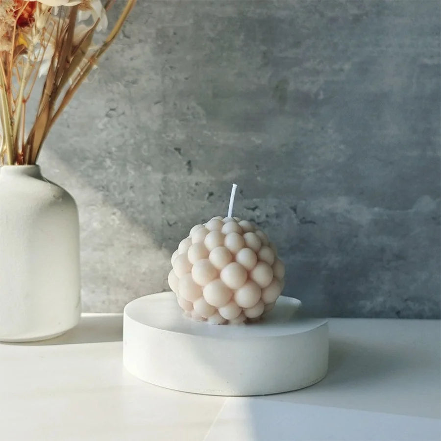 A white ceramic candle holder with a spherical cluster of white wax bubbles on a light surface.