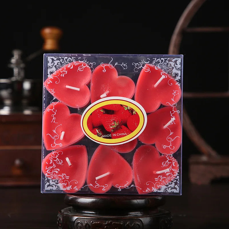 Un ensemble de bougies parfumées en forme de cœur rouges dans une boîte transparente, présentées sur un support en bois.