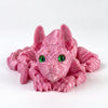 A pink articulated sphynx cat figurine with green eyes, shown in a close-up view.