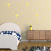 A bedroom wall decorated with gold star stickers and a wooden cabinet, next to a white bed.