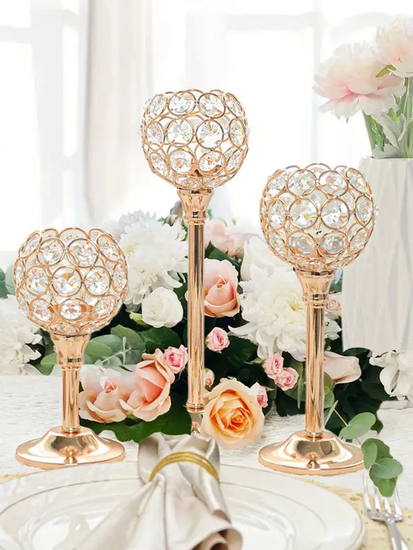 A set of golden crystal candle holders with floral designs arranged on a white table surrounded by pink and white roses.
