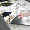 A hand touches a marble wall sticker featuring black and gold veining on a kitchen surface.