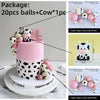 A pink and white cake decorated with cow-themed toppers, including balls and a cow figure.
