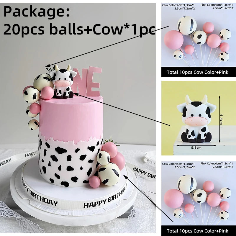 A pink and white cake decorated with cow-themed toppers, including balls and a cow figure.