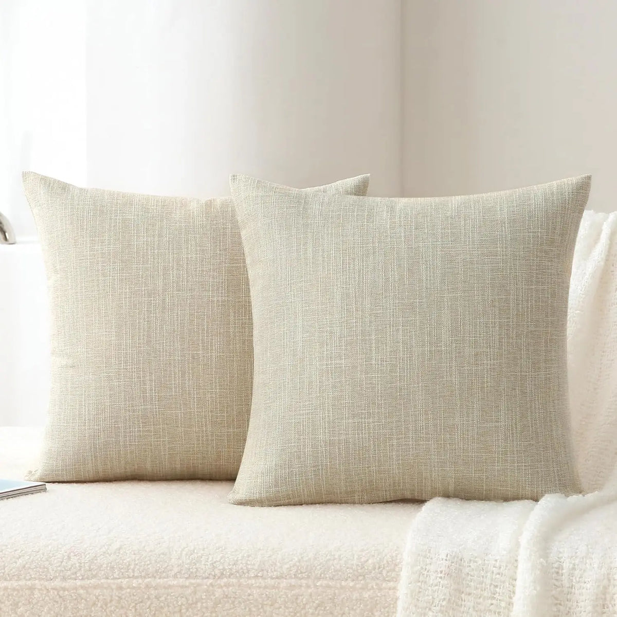 A set of two beige linen pillows resting on a white surface.
