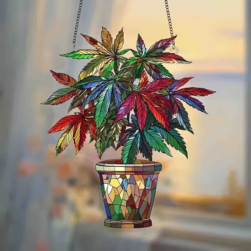 A pendant of a leafy green cannabis plant with variegated leaves hangs from a chain and rests in a colorful glass pot.