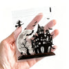 A hand holds a clear self-adhesive treat bag featuring a silhouette of a spooky castle and bats against a full moon backgroun