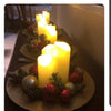 Three glass candles with flickering LED flames surrounded by greenery and festive decorations.