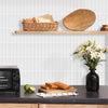 A wooden shelf displays bread and a large wooden cutting board against a white tiled wall.