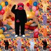 A plush monster costume in black with pink features is displayed among colorful balloons and pillows.