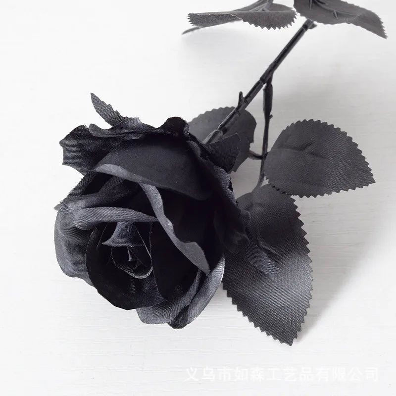 A dark black velvet artificial rose with a bendable stem on a white background.