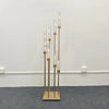 A tall gold metal candelabra set featuring eight slender glass candle holders arranged vertically.