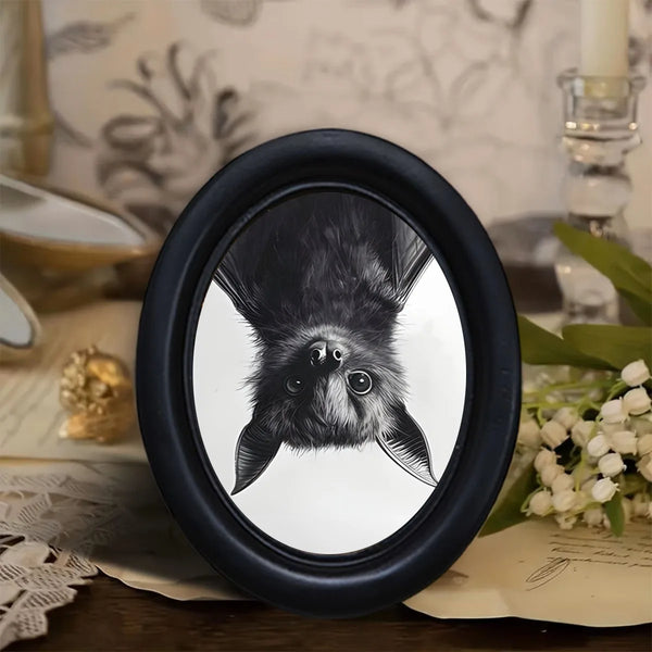Black oval frame featuring a black bat hanging decoration on a light background.