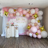 A pink and gold balloon garland arch decorated for a celebration with white and pink balloons and gold star accents.
