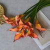 A bunch of orange and pink artificial calla lily stems displayed on a light gray surface.