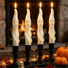 A set of four white soy candles shaped like ghosts and mummies displayed on a dark surface with autumn leaves.