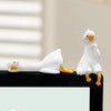 Figurine de canard en résine blanche avec des pattes jaunes, présentée sur une surface noire.