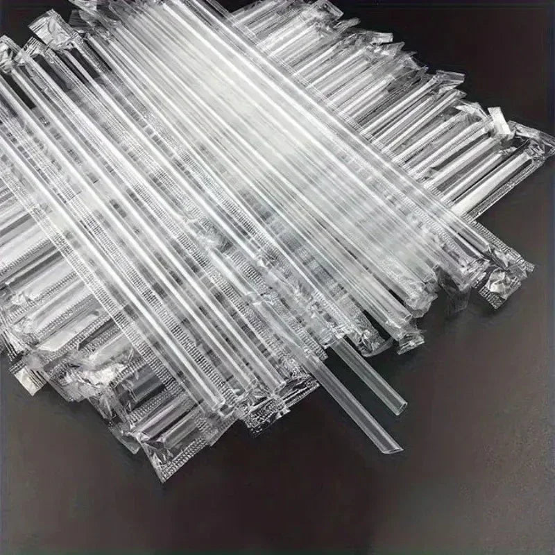A pile of clear disposable plastic straws arranged diagonally on a dark surface.