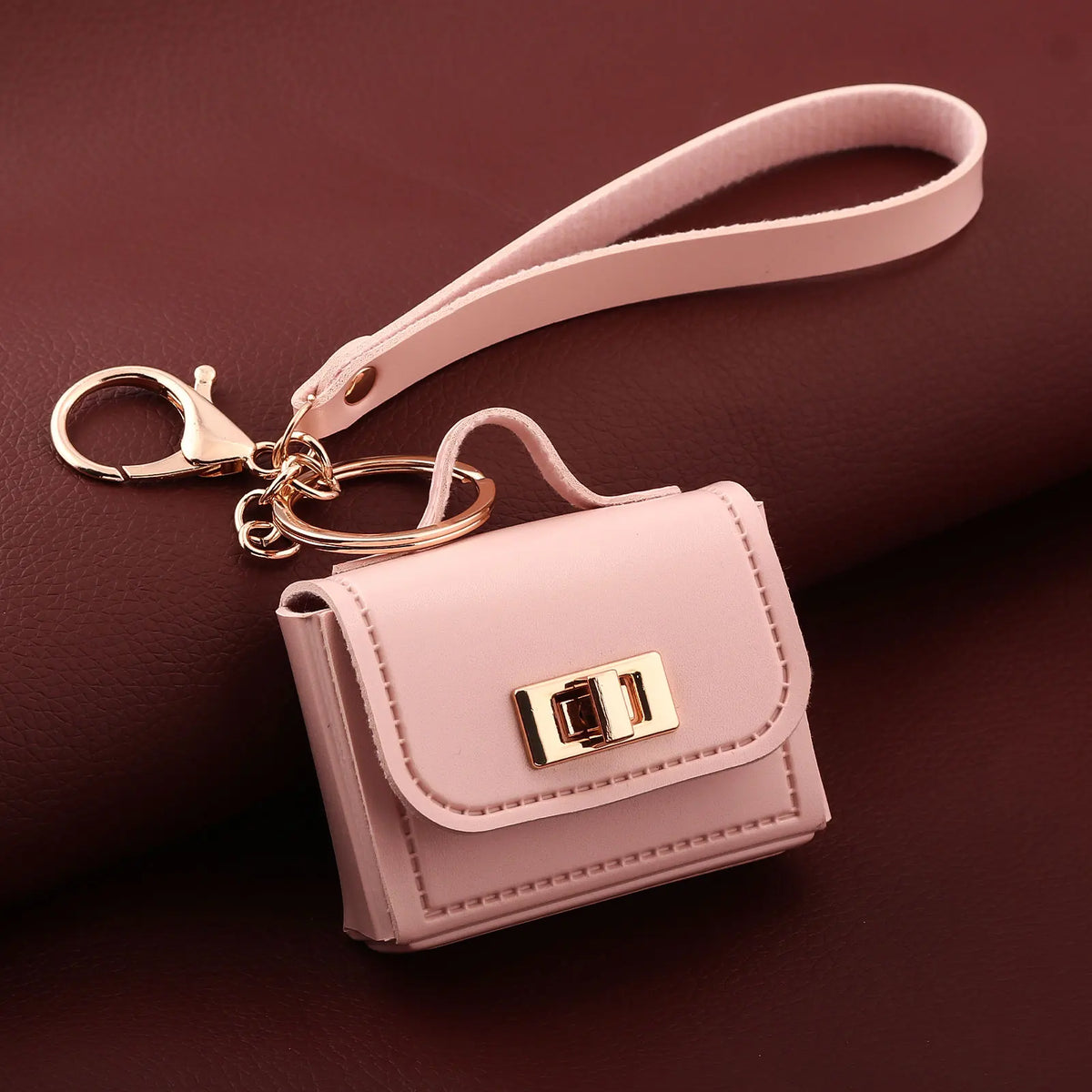 A pink mini leather openable bag with a gold chain and leather strap resting on a brown surface.