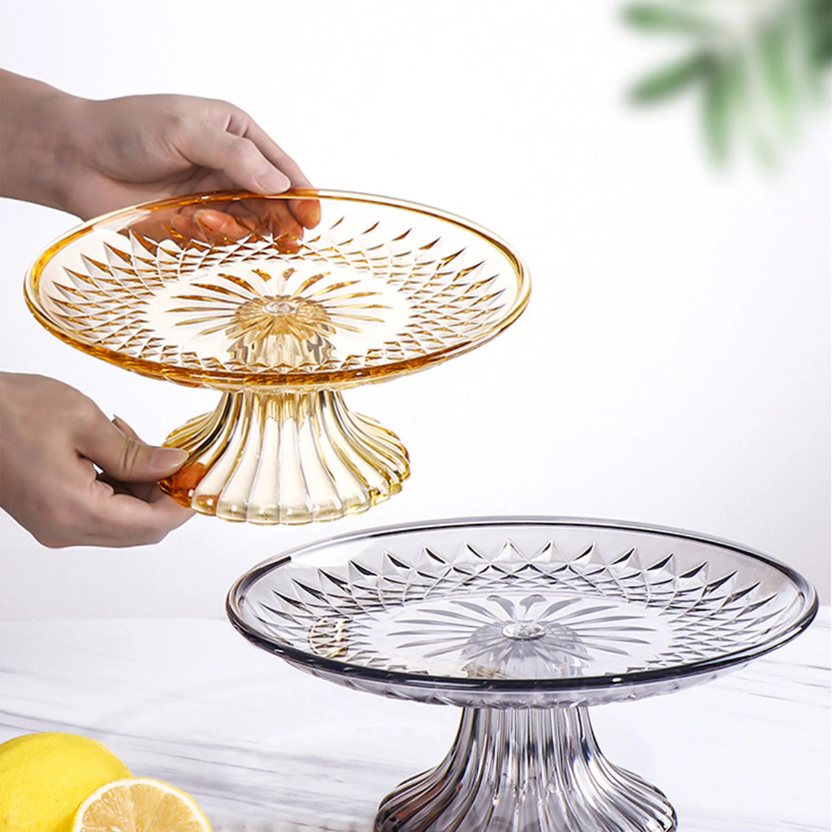 A hand is holding a clear acrylic serving plate for fruit or appetizers above another similar glass plate.