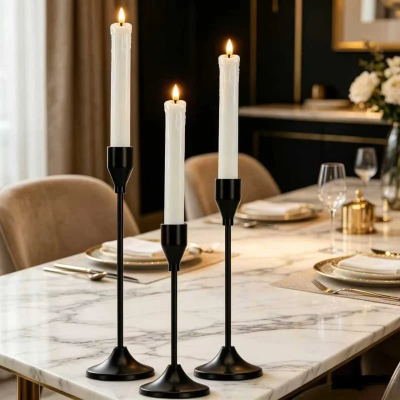 A set of black candle holders with white candles displayed on a marble table.