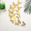 A set of twelve gold and brown 3D butterfly wall stickers displayed against a white background next to a green plant.