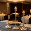 Three elegant gold metal candlesticks displayed on a table setting for wedding or holiday décor.