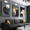 A set of three abstract marble geometry canvas art pieces featuring black, gold, and white textures displayed on a gray wall 