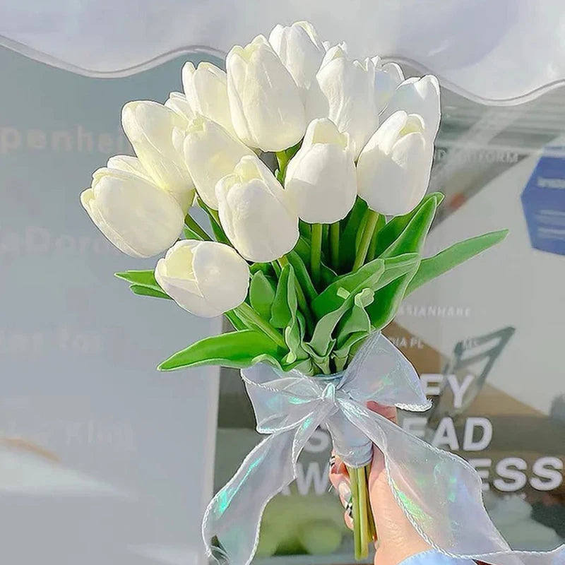 A bouquet of white artificial tulips wrapped with a sheer ribbon, held by a person.