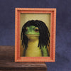 A cute green frog character is displayed inside a wooden photo frame.