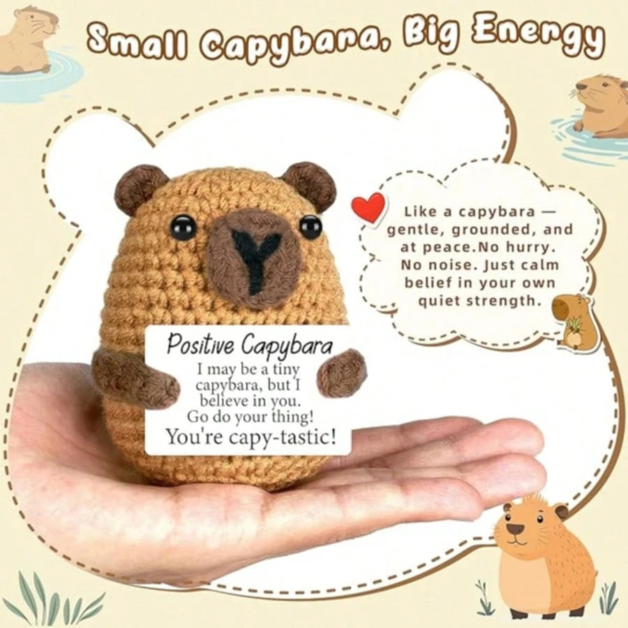 A hand-woven capybara plush pendant with an encouraging card is shown in a person's palm.