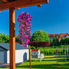 A vibrant purple and pink silk morning glory vine wreath hanging from a wooden structure against a clear blue sky.