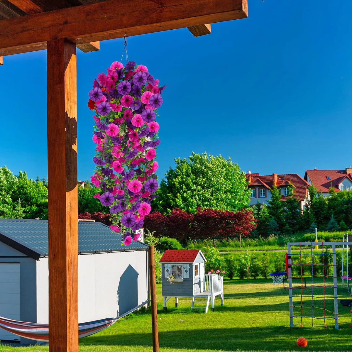 A vibrant purple and pink silk morning glory vine wreath hanging from a wooden structure against a clear blue sky.