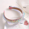 A pink LED glowing headband with iridescent accents is shown on a white surface.