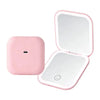 A pink portable folding LED makeup mirror with a reflective surface and a magnifying lens.