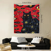 A tapestry wall hanging featuring a black cat with glowing yellow eyes against a red background with many other watchful eyes