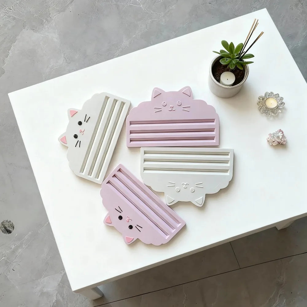 Pink and white cat-themed food bag squeezer tools displayed on a white table.
