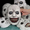 A close-up of a white demon mask with facial markings and large eyes, surrounded by other similar masks.