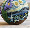 A colorful resin vase shaped like a landscape with swirling patterns and floral elements sits on a wooden surface.