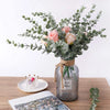 A bouquet of pink and peach roses and green eucalyptus leaves arranged in a glass jar