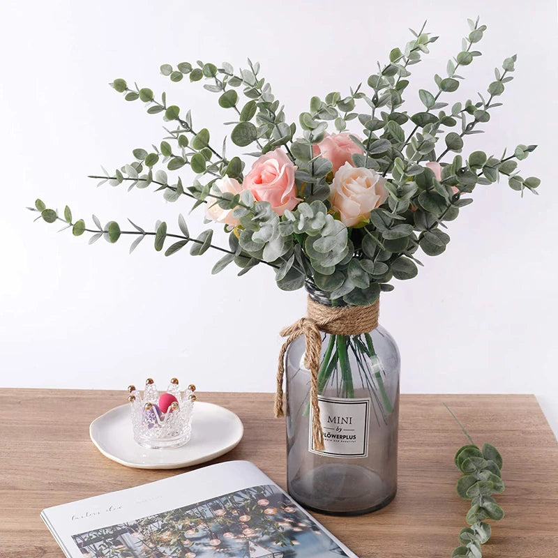 A bouquet of pink and peach roses and green eucalyptus leaves arranged in a glass jar