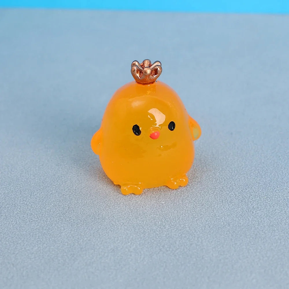A small, bright yellow resin chicken ornament with a gold crown and black eyes resting on a light blue surface.