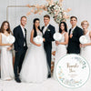 A group of ten people dressed in formal attire posing for a wedding photo surrounded by floral arrangements.
