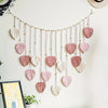 Handwoven pink leaf tassels hanging from a macrame cord against a white wall.