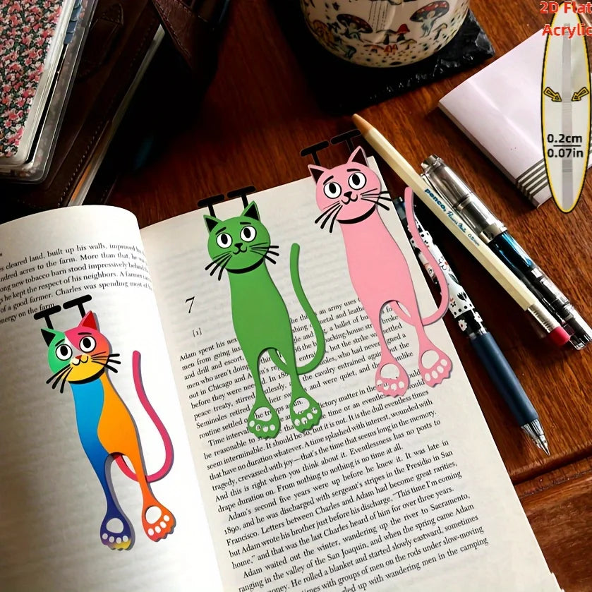 A close-up of a book featuring illustrations of three cats used as decorative bookmarks.