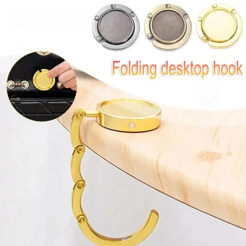 A gold-colored folding desktop hook is shown with a black fabric item, demonstrating its use as a portable purse hanger.